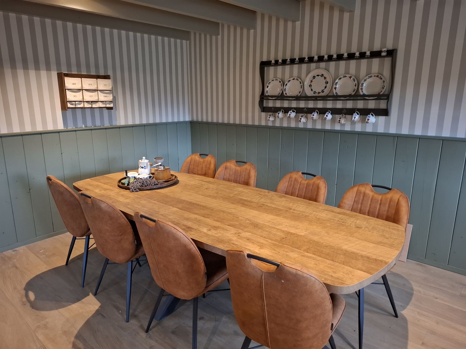 De lange eettafel met leren stoelen, met servies en een oude koffiemolen aan de wand