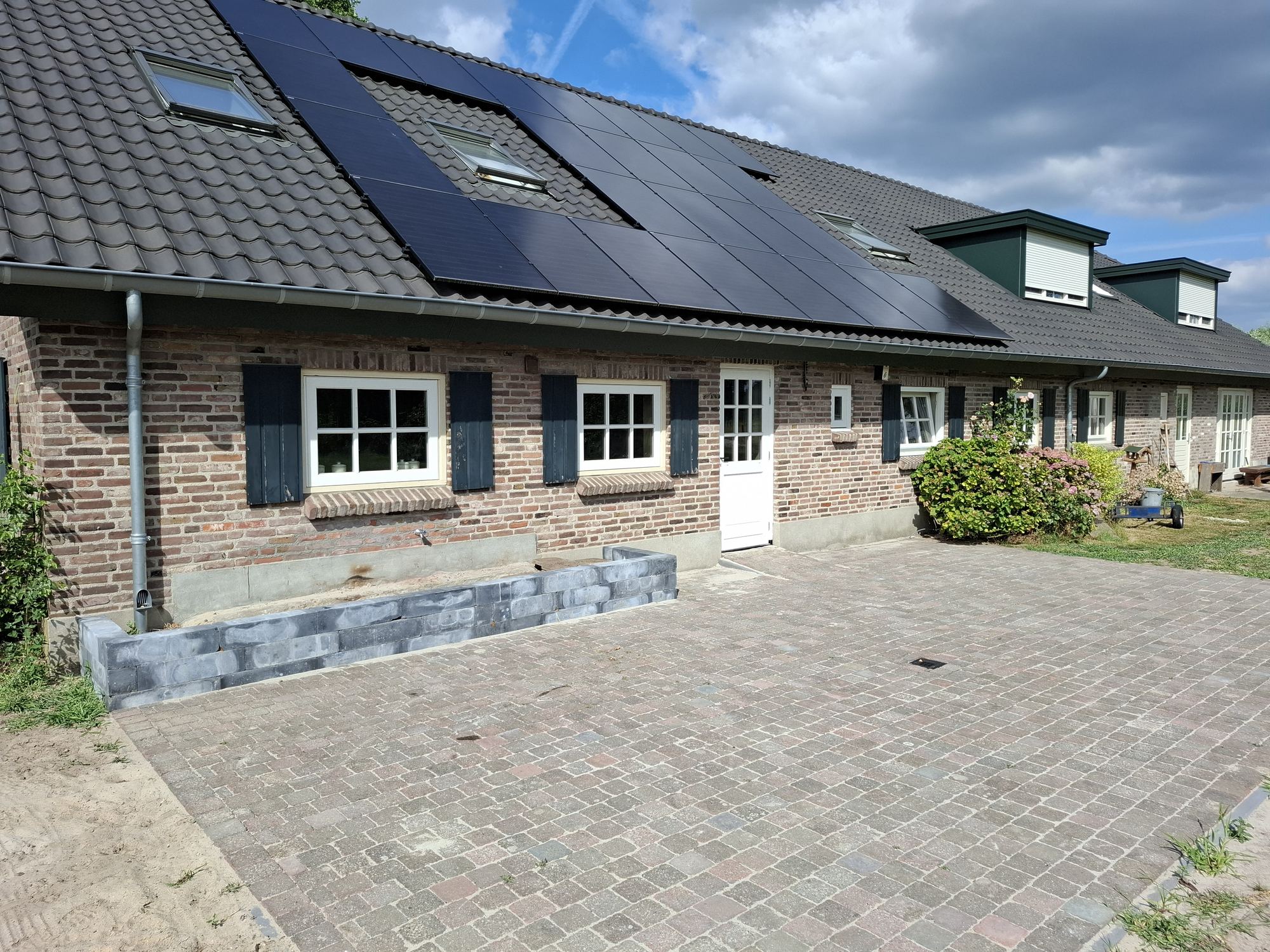 De voorzijde van de hoeve met zonnepanelen op het dak en een verhard erf