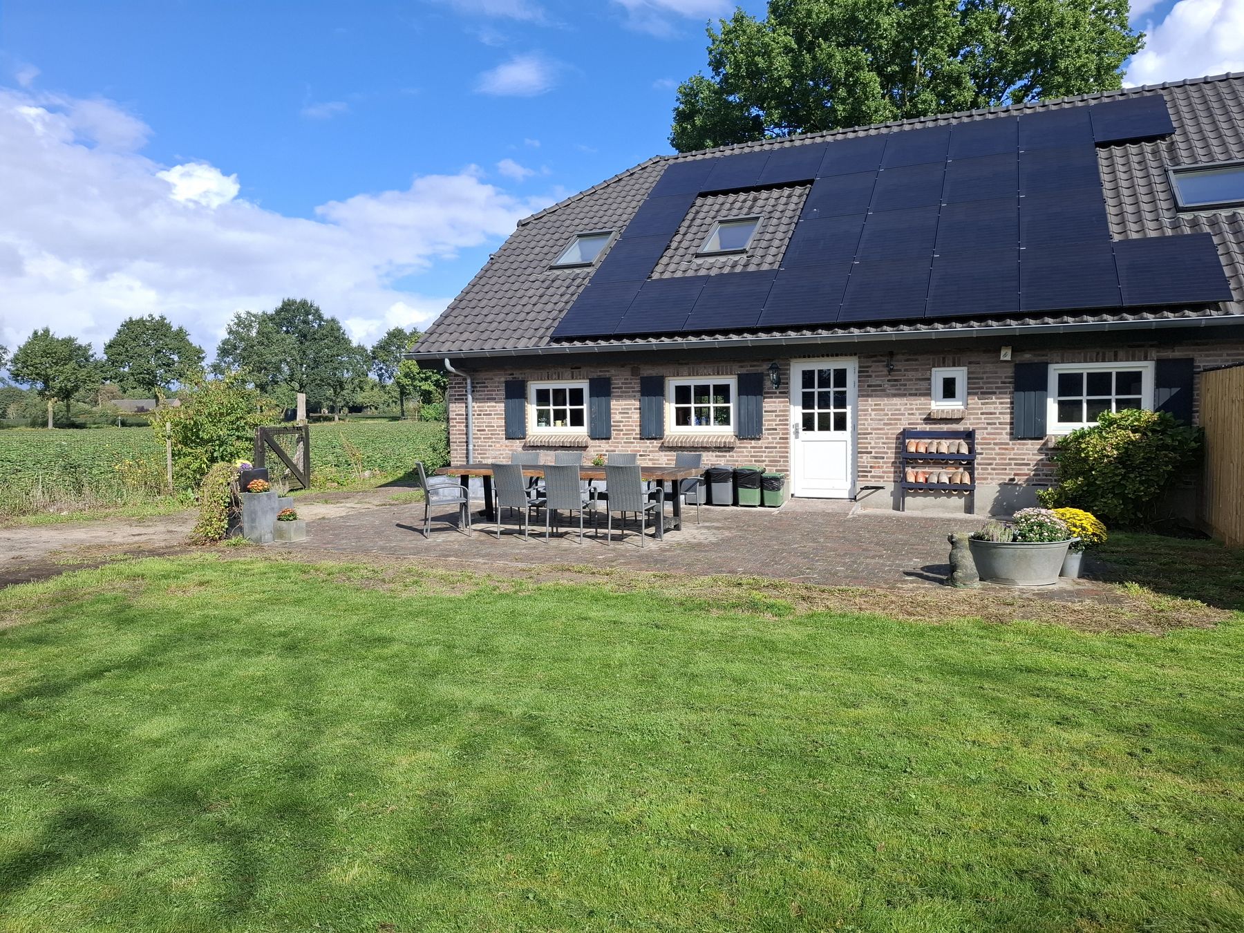 De Strijpse Hoeve in de zon: een baksteenboerderij met zonnepanelen, een terras met lange tafel en een ruim gazon